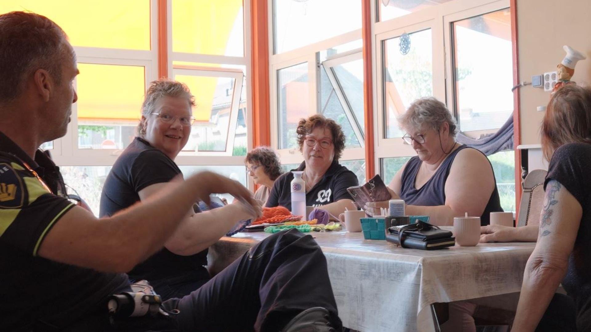 Een wijkagent in gesprek aan tafel met verschillende dames in een buurthuis. 