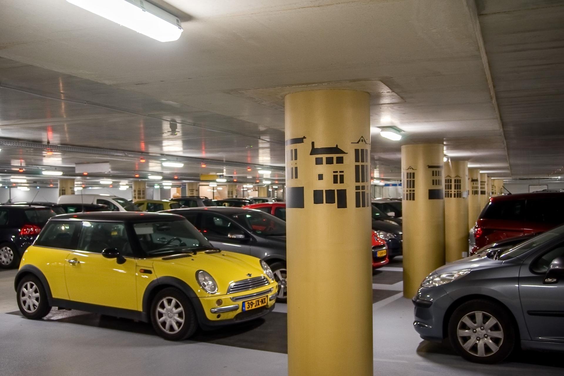 parkeergarage met allemaal geparkeerde auto's. De pilaren zijn goudkleurig met allemaal huizen erop.